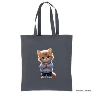 A dark gray tote bag features a cute, fluffy orange kitten wearing a blue hoodie and dark pants, standing upright with its paws together and big blue eyes looking forward. The background is plain and the bag has two long handles.
