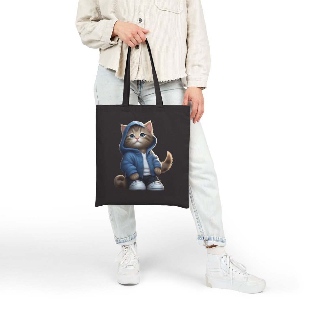 16484743616634768023_2048.jpeg Person holding a black tote bag with a cat in a blue hoodie design.