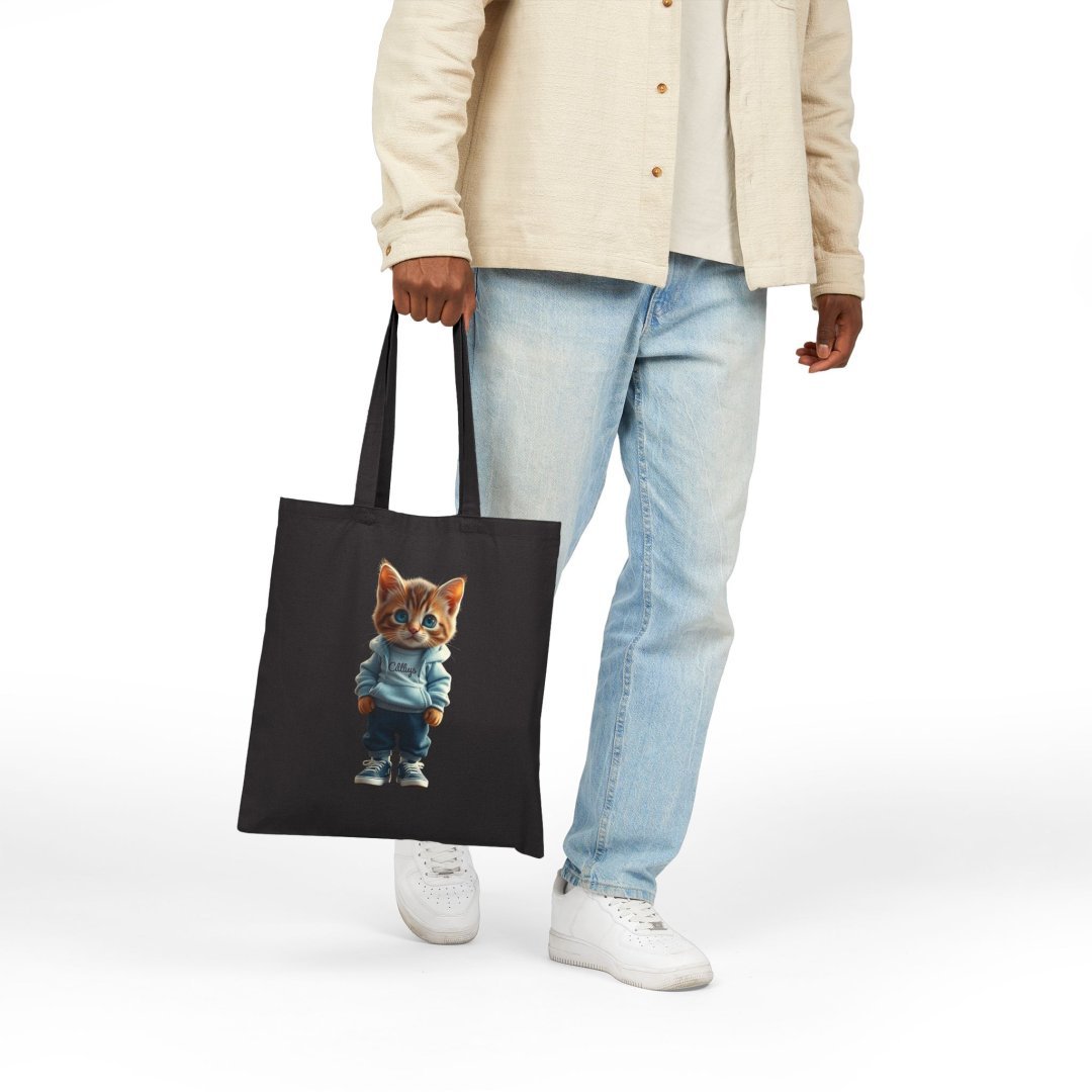 3574352614826925242_2048.jpeg Person holding a black tote bag with a cat in a hoodie design.