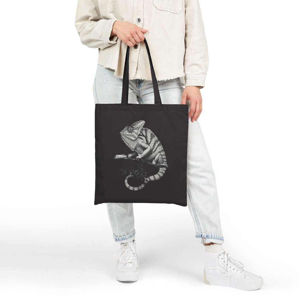 10675216892478290226_2048.jpeg Person holding a black tote bag with a chameleon design.