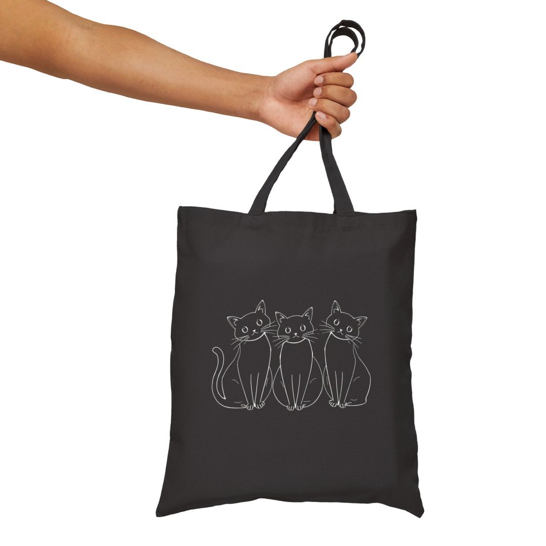 12985030431612070030_2048.jpeg Hand holding a black tote bag with three illustrated cats.