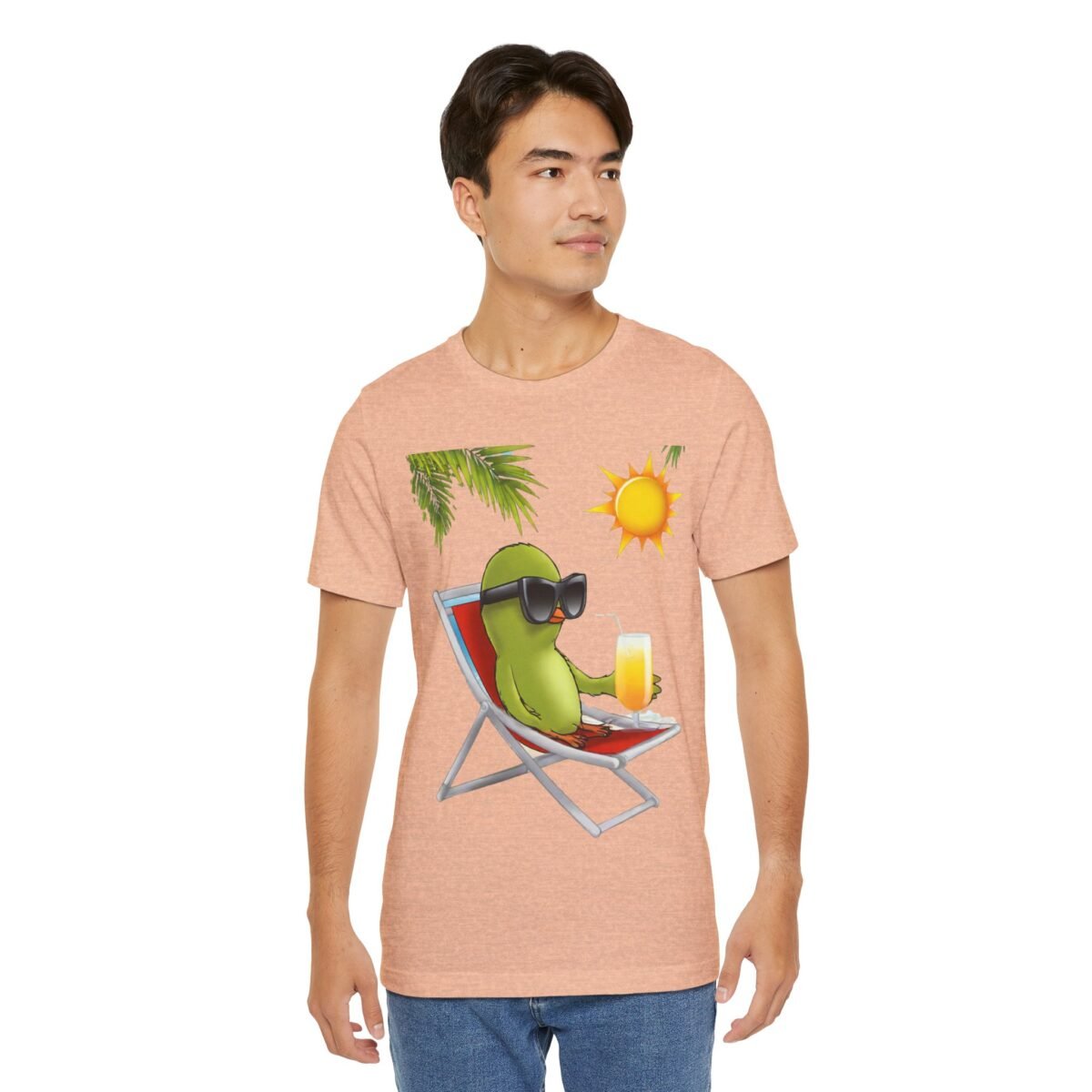 13001655206976948675_2048.jpeg A man in a peach t-shirt featuring a cartoon green bird with sunglasses relaxing in a beach chair.