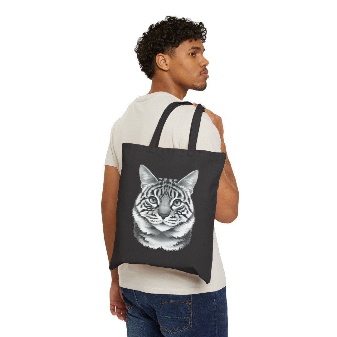13291980769255496380_2048.jpeg Man holding a black tote bag with a cat face design.