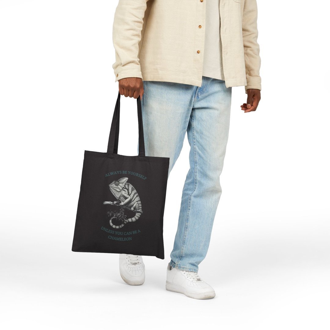 2360731950981835248_2048-1.jpeg Person holding a black tote bag with a chameleon design.