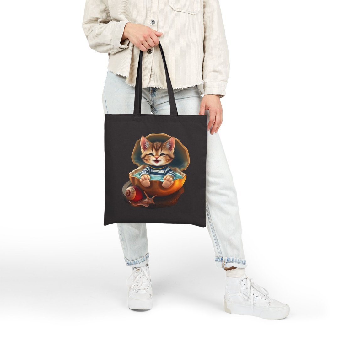 4656582654056803099_2048.jpeg Person holding a black tote bag with a cute cat design.