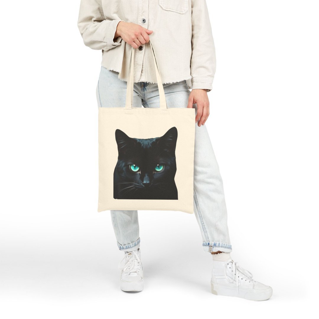 534589380655534530_2048.jpeg Person holding a tote bag with a black cat design.