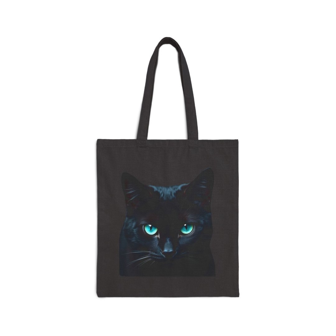 616626405895107039_2048.jpeg Black tote bag with a cat face design featuring striking blue eyes.