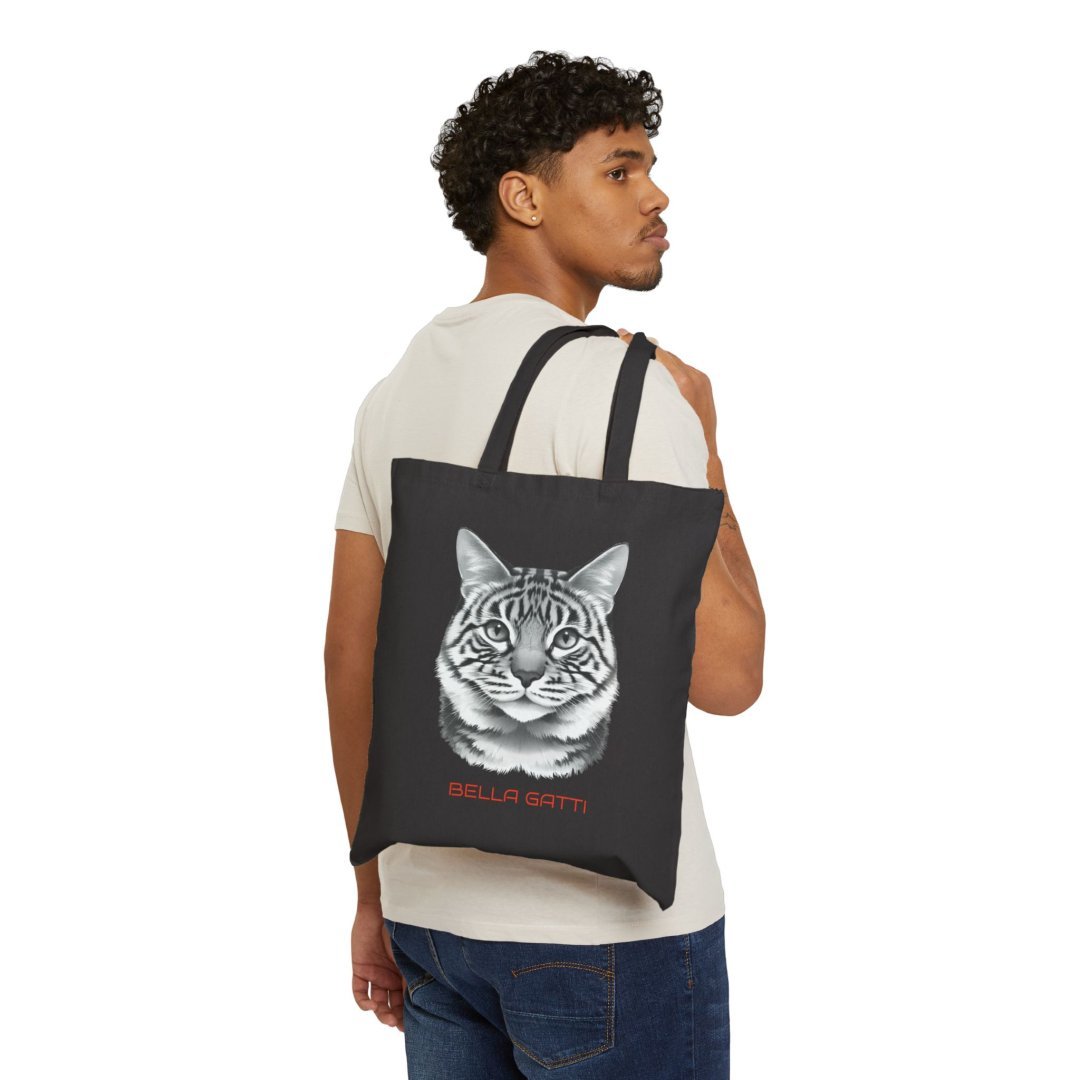 6479128624130555215_2048.jpeg Man holding a black tote bag with a cat face design and 'Bella Gatti' text.