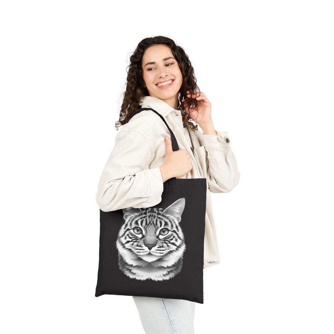 8085964676784607734_2048.jpeg Woman smiling and holding a black tote bag with a cat illustration.