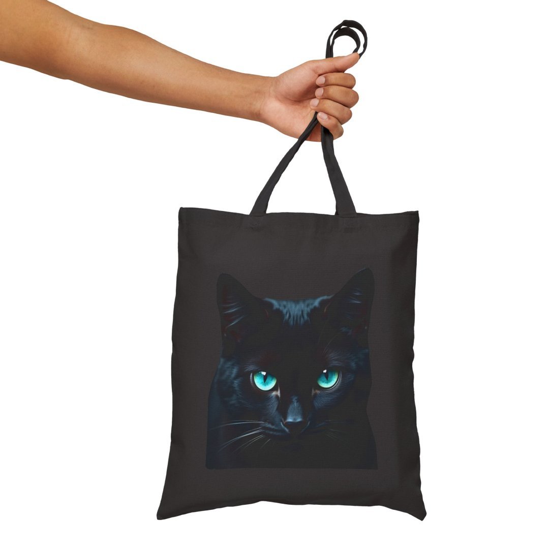 8370215288630195434_2048.jpeg Black tote bag with a cat face design and blue eyes.